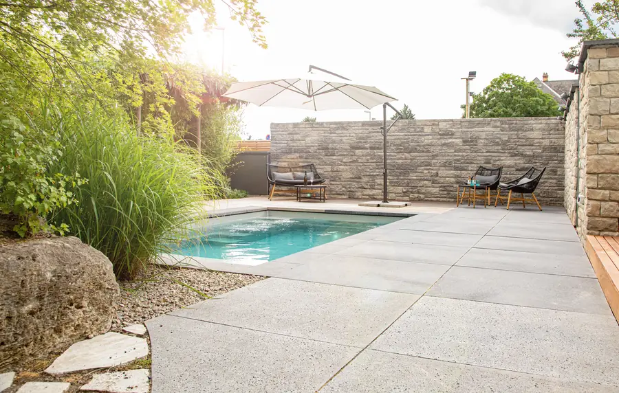 Poolterrasse mit Sonnenschirmen und Natursteinmauer im Abendlicht