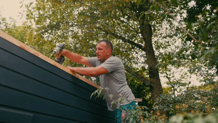 Mitarbeiter verschraubt eine Holzverkleidung an einem Gartenhaus