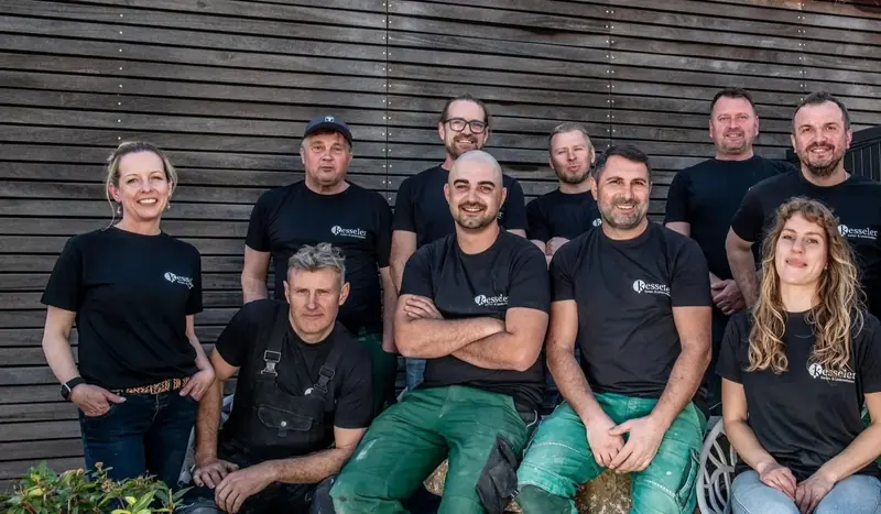 Das Team von Kesseler Garten- und Landschaftsbau, elf Personen vor einer Holzfassade